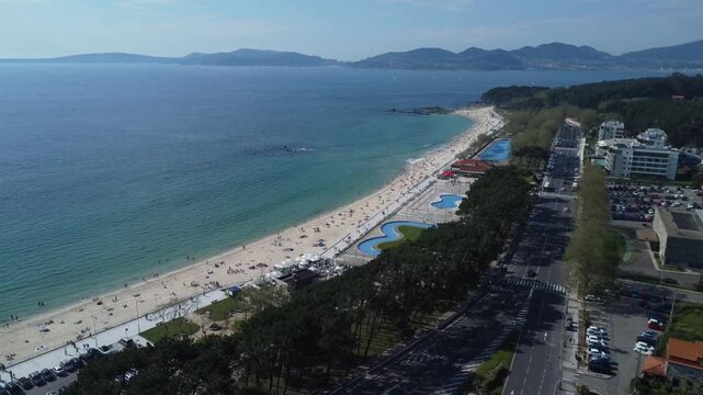 Aerial view of Playa de Samil, the main beach of Vigo in Galicia in northwest Spain. Sunny day, crystal clear blue sea. Houses, streets. Drone take.