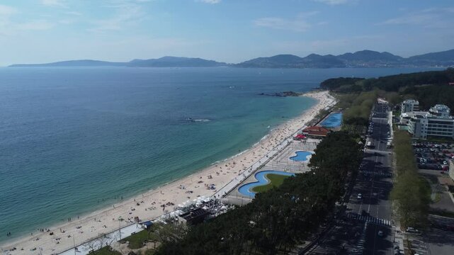 Aerial view of Playa de Samil, the main beach of Vigo in Galicia in northwest Spain. Sunny day, crystal clear blue sea. Houses, streets. Drone take.