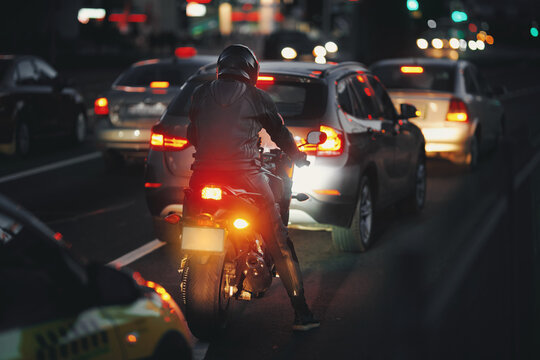 Motorbike rider waits in heavy evening traffic, vehicles on busy road with glowing headlights, ambient lights of the city. Night riding. Motorcyclist in full gear navigating crowded street at dusk