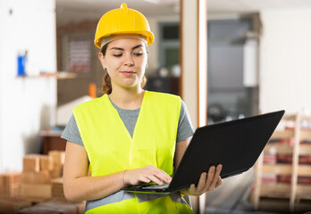 Focused young female architect in yellow protective workwear using modern software to create rooms design while standing in house under reconstruction