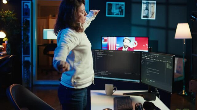 Programmer doing software quality assurance, stretching arms behind back after reading source code, feeling fatigued. IT expert takes break from work to relax muscles after inspecting coding, camera B