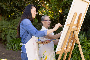 Naklejka premium Painting on canvas, Asian granddaughter and grandmother enjoying outdoor art session together