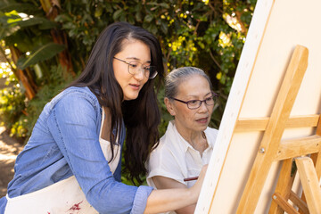 Naklejka premium Painting on canvas, asian granddaughter and grandmother enjoying outdoor art activity