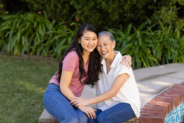 Naklejka premium Smiling asian woman and asian grandmother sitting outdoors, hugging and enjoying time together