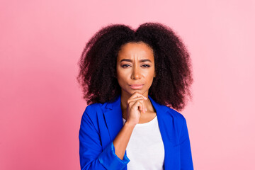 Portrait of smart intelligent pensive girl with wavy hairstyle dressed blue jacket holding hand on chin isolated on pink color background