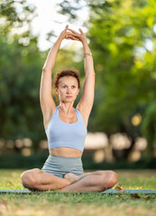 Woman practicing hatha yoga in summer garden, stretching in an asymmetrical seated asana Parivritta...