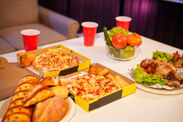 An indoor office party scene with no people around, featuring a desk filled with food pizza, bread, salad, chicken grill, French fries, and beerset against a night light with RGB lighting.