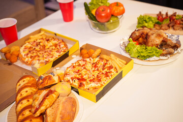 An indoor office party scene with no people around, featuring a desk filled with food pizza, bread, salad, chicken grill, French fries, and beerset against a night light with RGB lighting.