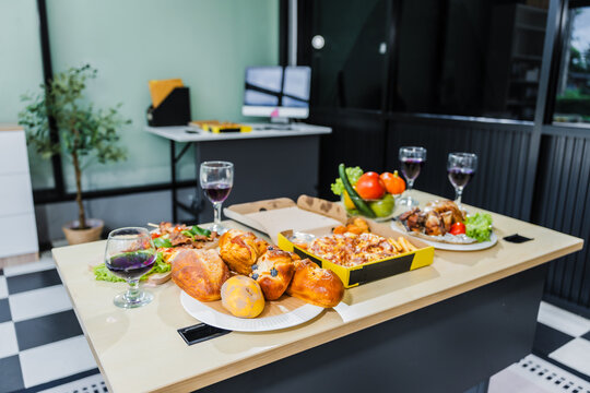 A business office is set for a Halloween party, with food spread across a desk pizza, bread, chicken grill, French fries, salad, and beer ready for celebration, but no people present.