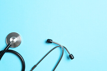 Stethoscope on light blue background, top view. Space for text