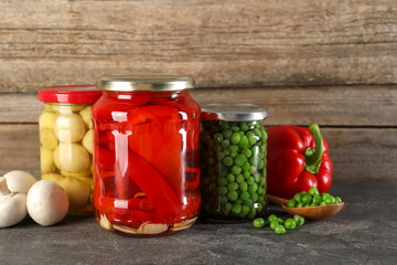 Different pickled products in jars on grey textured table