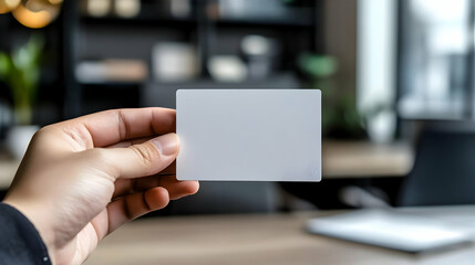 Hand holding a blank white card with a blurry office background.