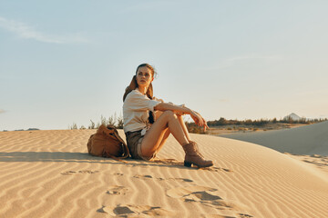 Woman sitting on sand dune with bag on shoulder, enjoying solitude and beauty of desert landscape