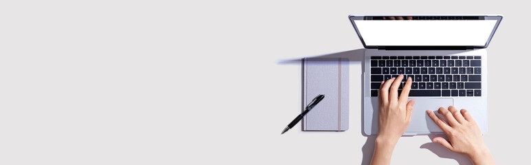 Person using a laptop computer with a notebook - Flat lay