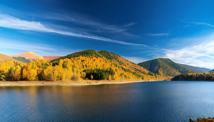 Naklejka premium A panoramic view of a forest with autumn leaves, a river, and blue sky in the background.