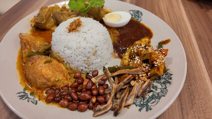 Asian food Nasi Lemak is a rice dish infused with coconut milk. Served with sambal, curry chicken, fried peanut, boiled egg and fried anchovies.