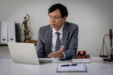 A senior man lawyer conducts an online consultation from a laptop via video link for a client. work...