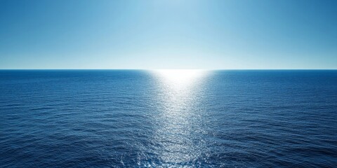 A bright blue sky and a vast expanse of sparkling blue ocean with a sliver of sunlight reflecting on the water.