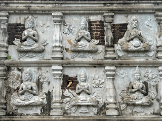 Close up details of temple relief and engravings depicting the Lord Buddha stories sculpted on white stones, decaying outdoor.