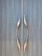Unique luxurious door made of black wood timber and bronze copper stainless steel frame material, with curved unique copper door handle to resemble ethnic or local culture.