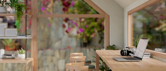 A laptop on a wooden table by the window in a contemporary Scandinavian coffee shop seating area.