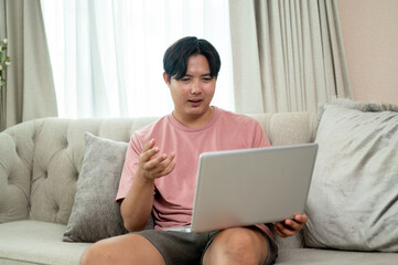 Fototapeta premium An Asian man is working remotely from home, having an online meeting via laptop with his colleagues.