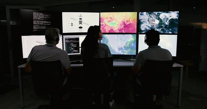 People, control room and team monitor satellite maps to track storm weather pattern with back. Meteorologist, climate scientist or group on screen with ai code for global warming at night on overtime