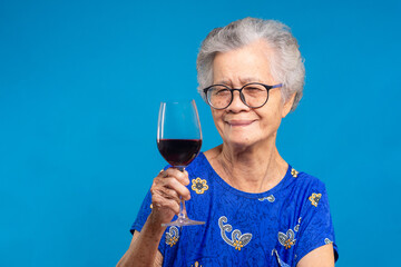 Senior woman enjoying red wine in blue dress, symbol of relaxation and joy
