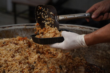 The chef puts the finished pilaf from the cauldron into a plastic cup.