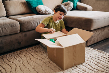 Happy cheerful kid boy packing his toys for delivery donation box. Charity and recycling