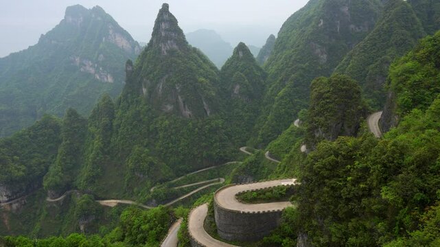 Winding road in lush green mountains of Tianmen Mountain on a misty day, China