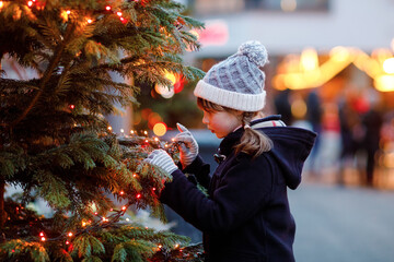Little cute kid girl having fun on traditional Christmas market during strong snowfall. Happy child...