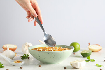 Sweet potato puree in bowl, spoon in hand, garlic and lime on light background