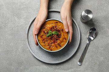 Mashed sweet potatoes with spices in bowl and hands on gray background, top view