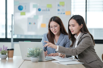 Two women are sitting at a desk with a laptop and a notebook