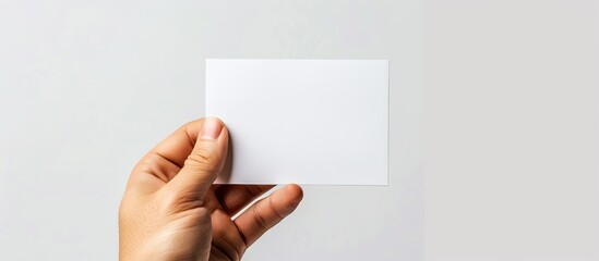 Fototapeta premium An empty white paper card is held in hand against a white background. Copy space image. Place for adding text and design