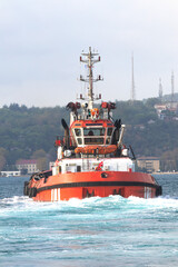 Fototapeta premium Orange tugboat sailing in the Bosphorus. The pilot boat leaves leaving foam behind. Marine craft idea concept.