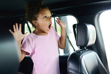 Child in a car expressing surprise or excitement with hands rais