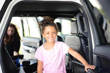 Smiling child inside a car with an adult cleaning in the backgro
