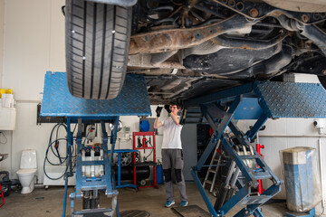 car mechanic standing under lifted car and fixing car in garage