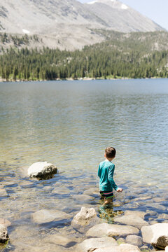 Boy standing in shallow lake water with mountains in background