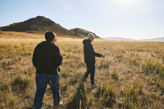 Two people walking in a grassy field with hills in the background.