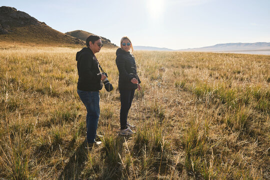 Two people walking in a grassy field with hills in the background.