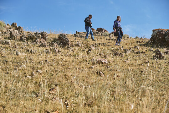 Two people hiking on a rocky hillside under a clear blue sky.