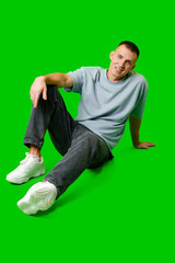 Casual Young Man Sitting on Floor in Comfortable Clothes With Green Background