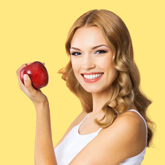 Portrait of happy smiling cute woman holding red apple, isolated yellow background. Blonde girl in healthy eating, dieting and dental care, stomatology studio ad concept. Square image.