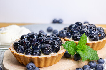 Close-up of blueberry tartlets on a small cutting board. blueberries around and mascarpone on the back