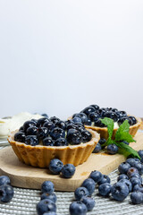 Blueberry tartlets on a small cutting board. blueberries around and mascarpone on the back close-up