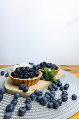 Blueberry tartlets on a small cutting board. blueberries around and mascarpone on the back