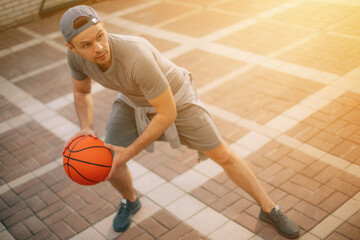 A man in a backward cap and athletic wear is in a low, wide stance while holding a basketball,...